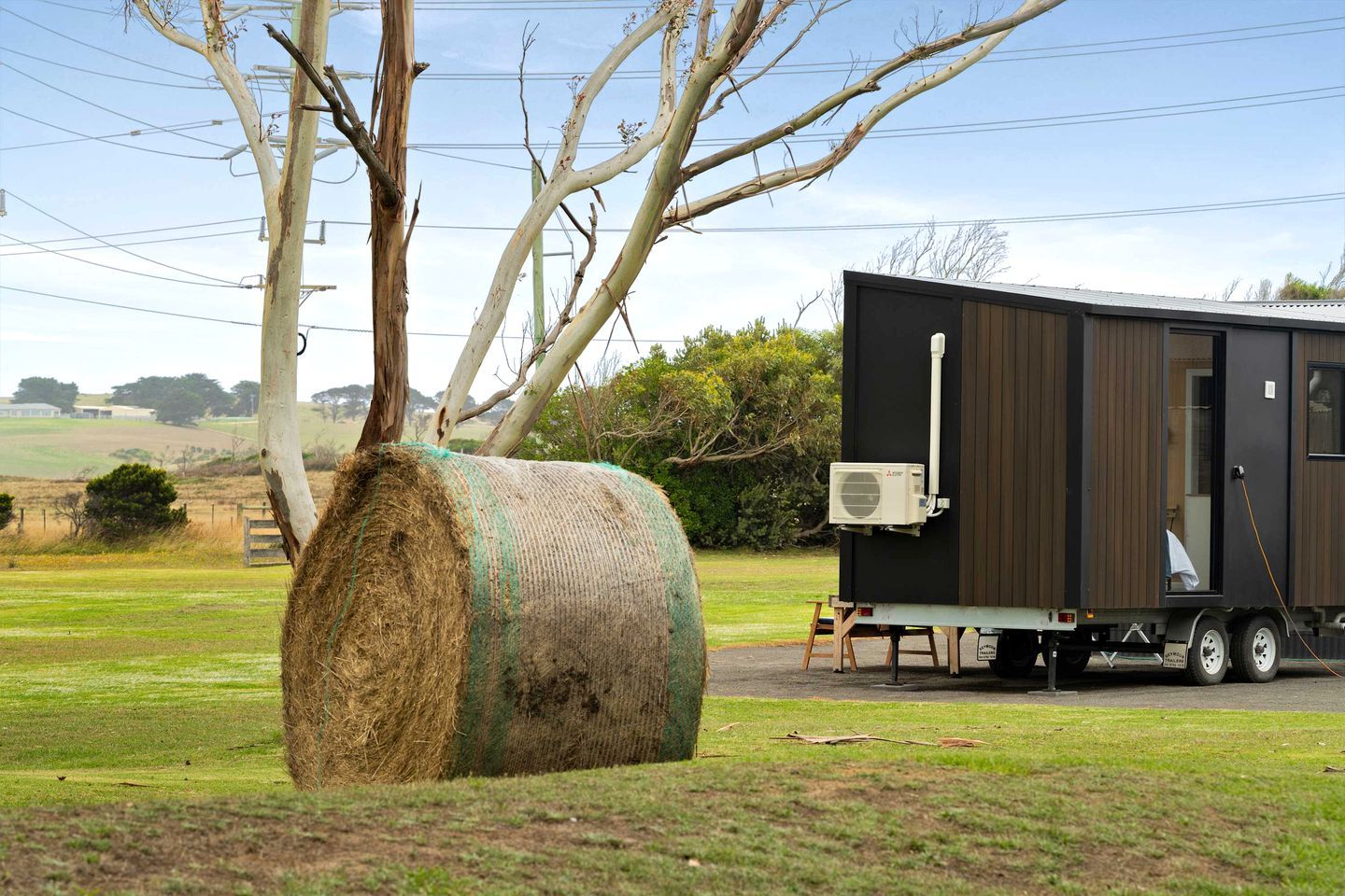 Une maison mobile avec une grande botte de foin, située dans un cadre rural.