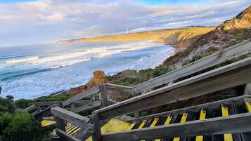 A coastal view with a wooden staircase leading down to the beach, overlooking the ocean and wind turbines in the distance.