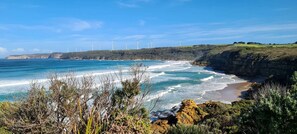 A coastal landscape with a beach, ocean waves, and wind turbines in the distance.