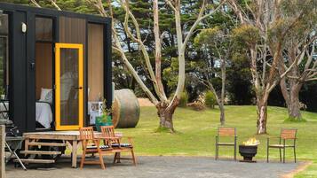 A modern cabin with a sliding door, a dining area with a table and chairs, and a fire pit.