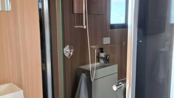 A modern bathroom with a glass shower enclosure, a white sink, and a towel hanging on the wall.