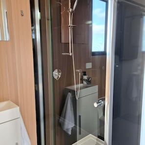A modern bathroom with a glass shower enclosure, a white sink, and a towel hanging on the wall.
