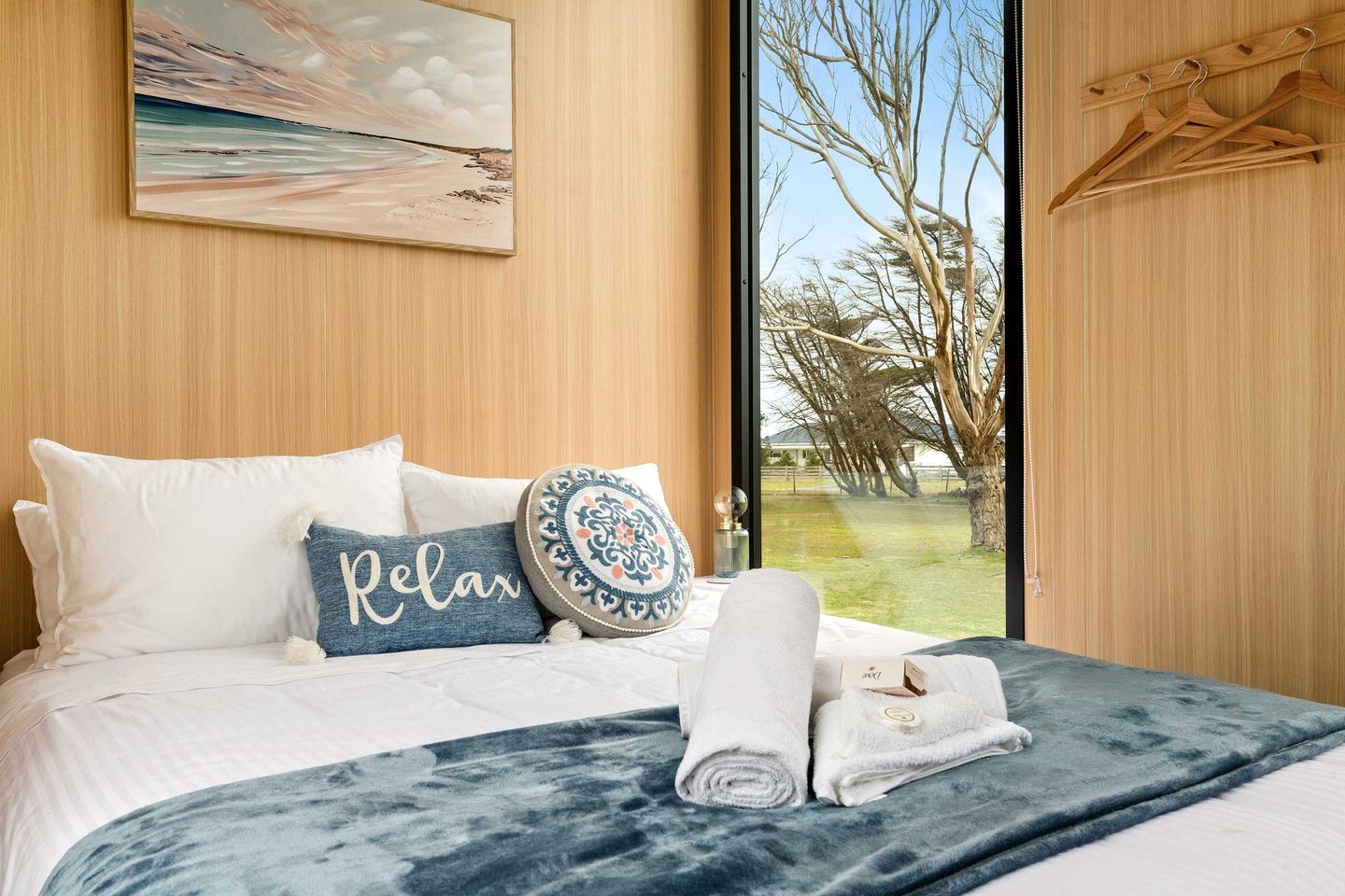 A bedroom with a bed, pillows, a blue blanket, and a view of trees through a window.