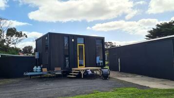 A modern, compact building with a flat roof, a door with a yellow frame, and a small outdoor seating area with a table and chairs.