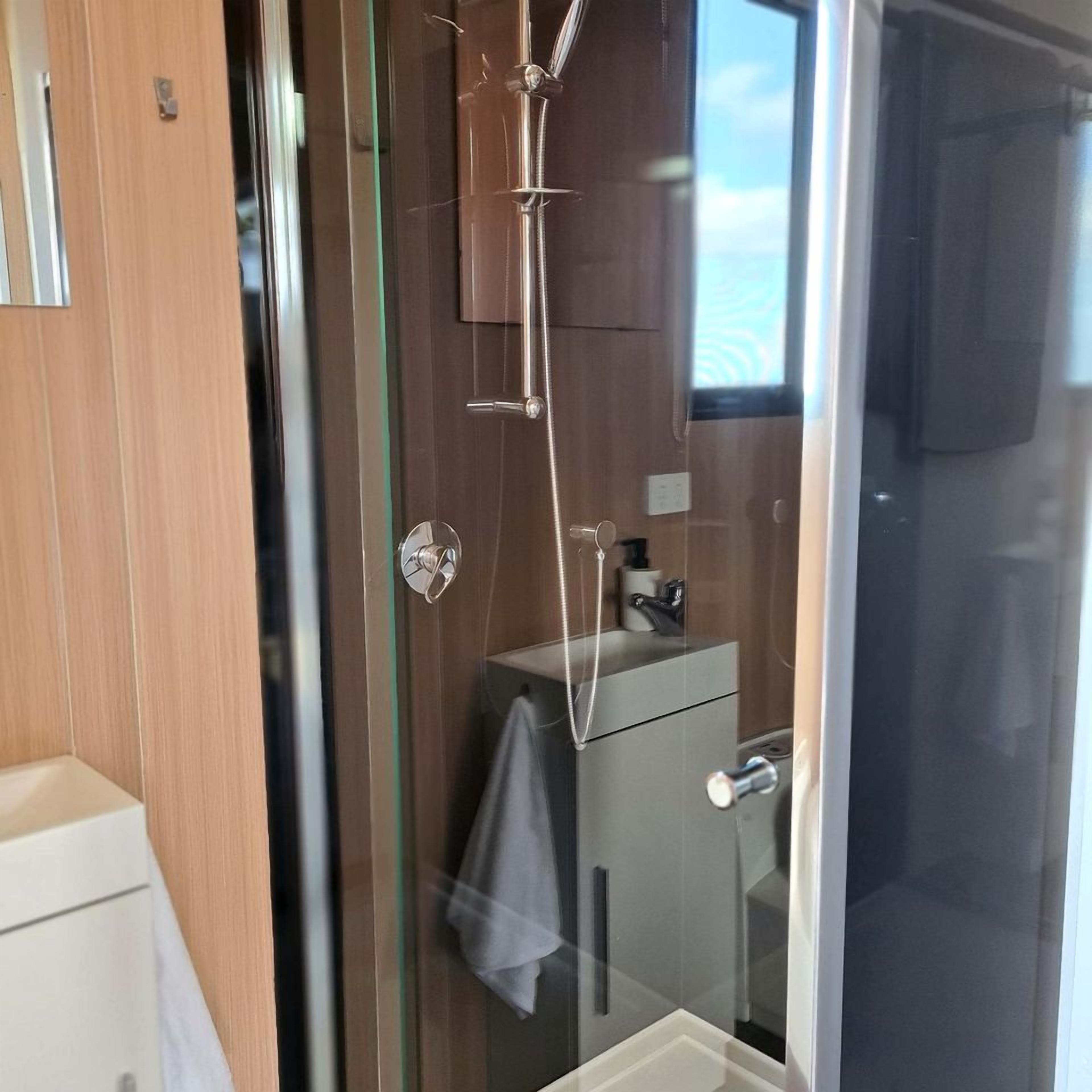 A modern bathroom with a glass shower enclosure, a white sink, and a towel hanging on the wall.