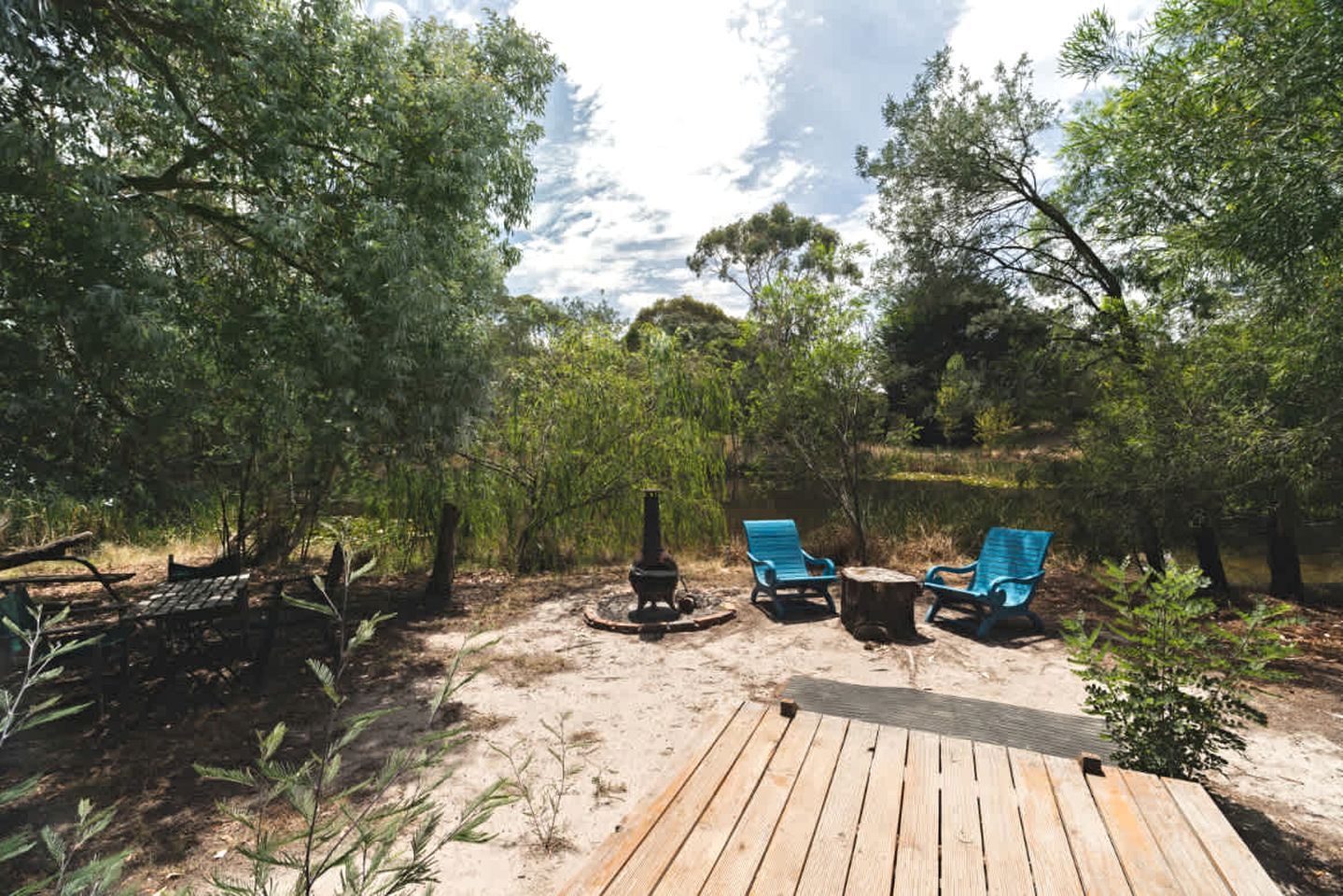 A deck with two blue chairs and a fire pit in a wooded area.