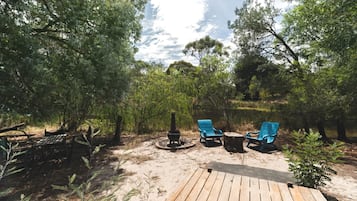A deck with two blue chairs and a fire pit in a wooded area.