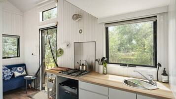 Cocina compacta con estufa a gas, lavamanos y ventana con vista a la vegetación.