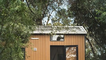 Une petite cabane en bois avec une porte et des fenêtres, deux chaises bleues et une table.