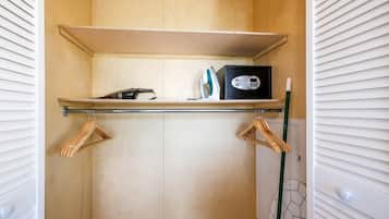 A wooden closet with a shelf, a black safe, and wooden hangers.