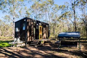 A small cabin with a wooden exterior, a yellow door, and a covered outdoor seating area.