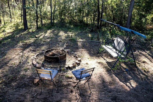 A campsite with a fire pit, two chairs, and a hammock.