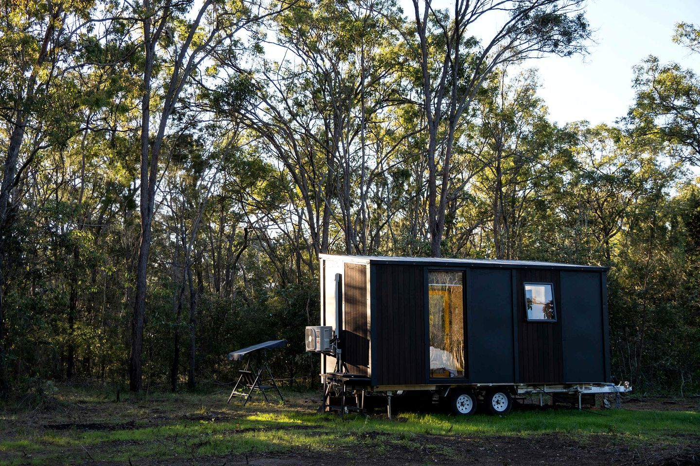 A mobile home in a wooded area with a trailer bed, a small porch, and a window.