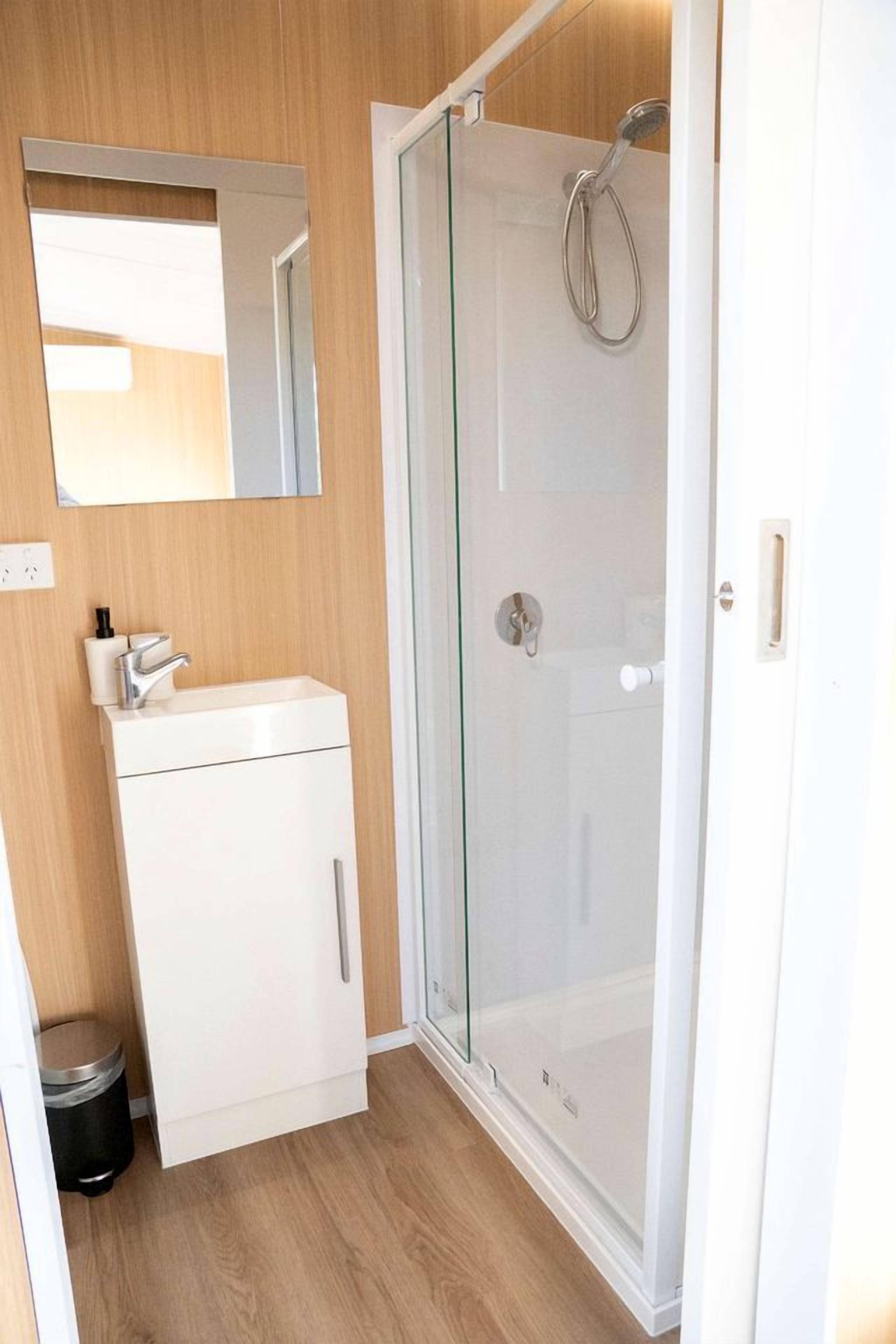 Une salle de bain avec une douche à parois de verre, un lavabo blanc et un miroir au mur.