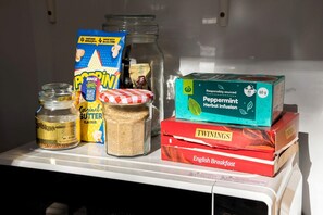 A refrigerator stocked with food items including a jar of butter, a bag of popcorn, a box of Binge Binge popcorn, a box of peppermint herbal infusion, and a box of Twinings English Breakfast tea. - Serene Tiny Home Retreat with Wildlife Farm Stay Near Hervey Bay, Queensland (Howard)