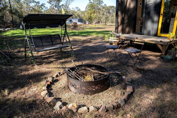 An outdoor seating area with a fire pit, a swing, and a deck with chairs.