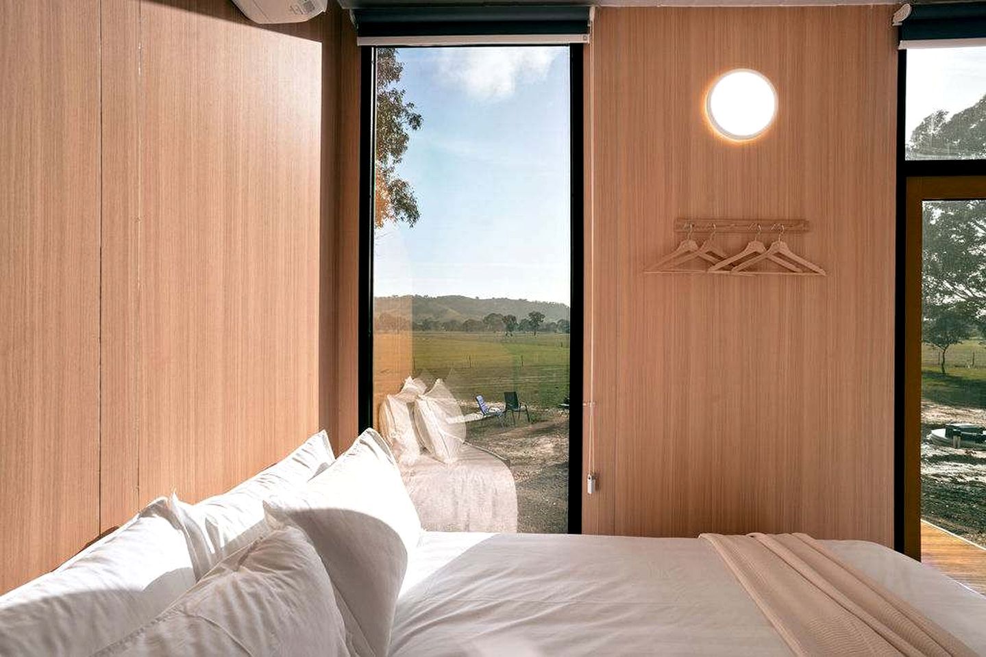 Ein Schlafzimmer mit einem Bett, einem großen Fenster und Blick auf ein grünes Feld.