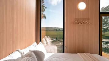 A bedroom with a bed, a large window, and a view of a grassy field.