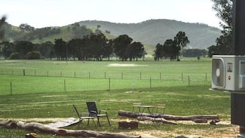 A grassy field with a fence, chairs, and a fan.