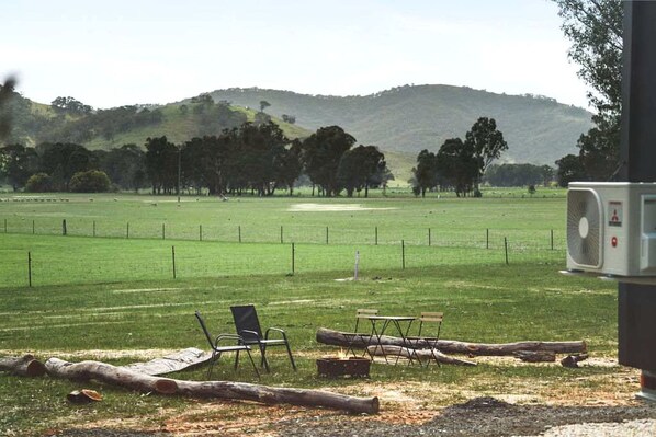 A grassy field with a fence, chairs, and a fan.