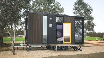 Una cabaña pequeña y moderna con puerta corredera, ventana y rampa metálica que lleva a la entrada.