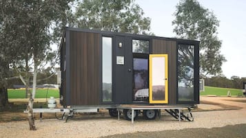 Una cabaña pequeña y moderna con puerta corredera, ventana y rampa metálica que lleva a la entrada.