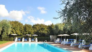A swimming pool with lounge chairs and umbrellas, surrounded by greenery.