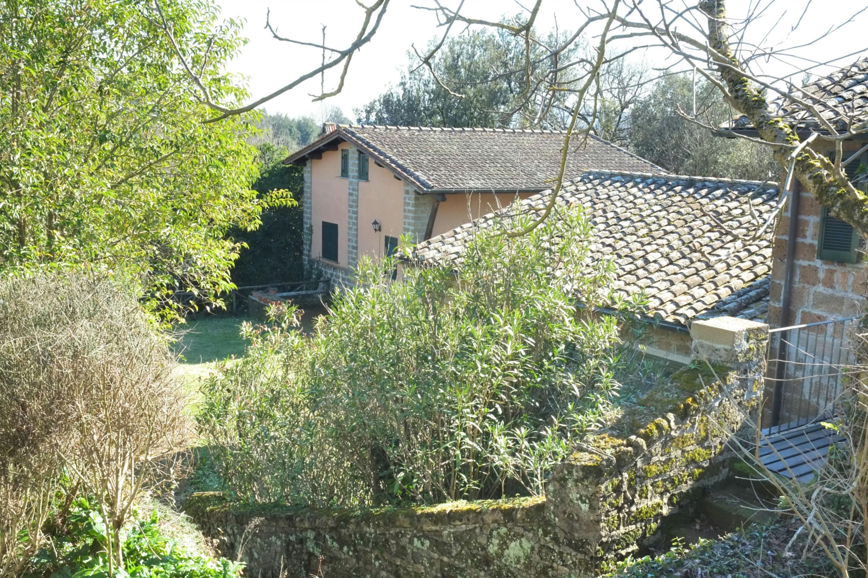 A traditional stone building with a tiled roof, surrounded by lush greenery and trees.