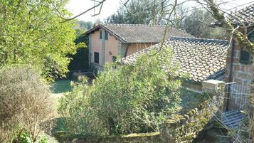 A traditional stone building with a tiled roof, surrounded by lush greenery and trees.
