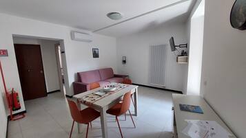 Ett kompakt bostadsutrymme med ett matbord, två stolar, en soffa, ett element och en brandsläckare.