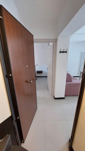 Ett modernt hotellrum med en trädörr, vita väggar, en rosa soffa och ett litet sidobord.