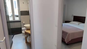 Ett hotellrum med en säng, ett sängbord, ett badrum med toalett och handfat samt en dusch.