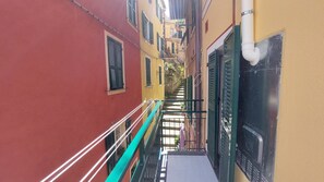 Ein schmaler Gang mit einer Treppe, die zu einem Gebäude mit einem grünen Geländer und einer weißen Rohrleitung führt.