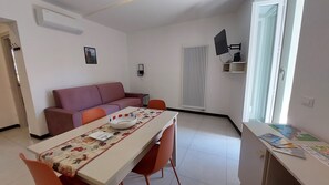 Ett modernt vardagsrum med en soffa, ett matbord med stolar, en tv som är monterad på väggen och ett element.