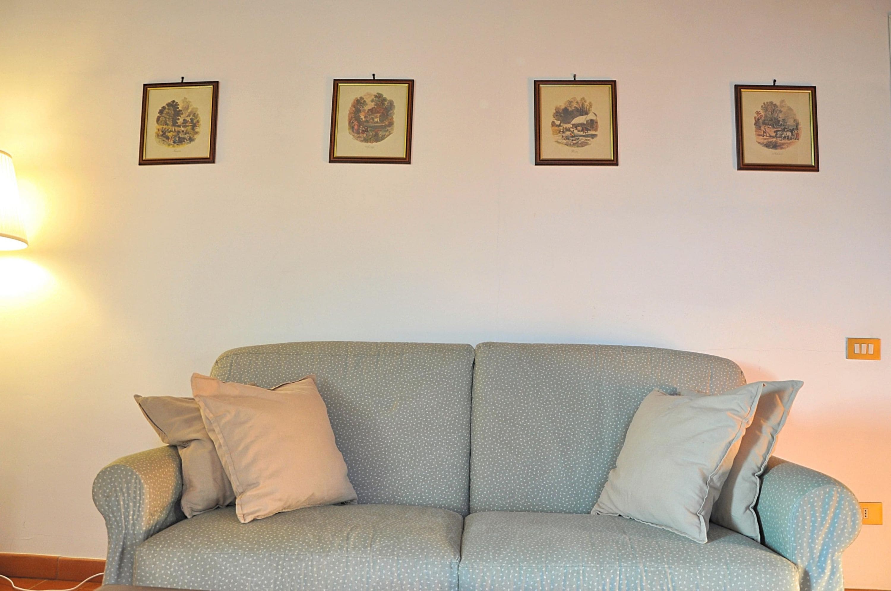A living room with a sofa, four framed pictures on the wall, and a lamp.