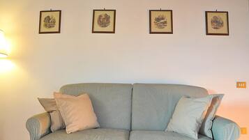 A living room with a sofa, four framed pictures on the wall, and a lamp.