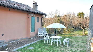 A small patio with a table and chairs, a white umbrella, and a building with a tiled roof.