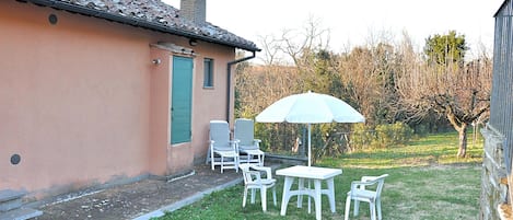 A small patio with a table and chairs, a white umbrella, and a building with a tiled roof.
