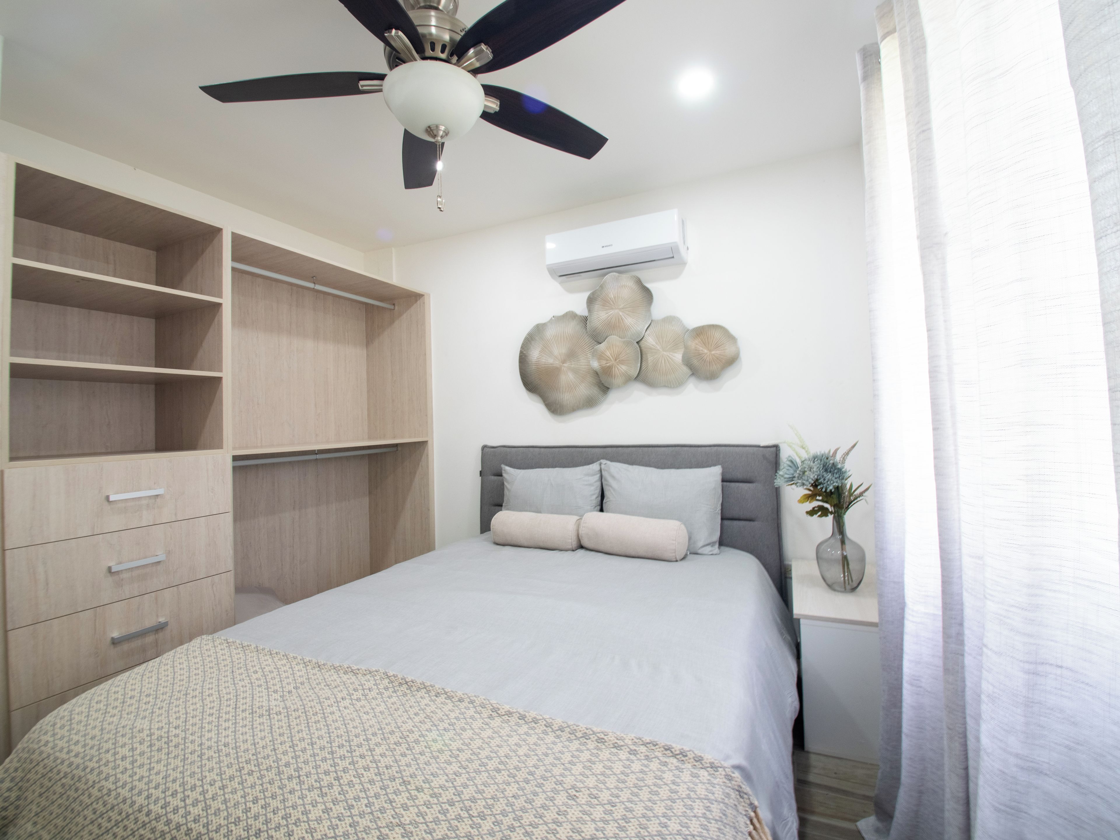 A bedroom with a bed, a wardrobe, a ceiling fan, wall art, and a window with curtains.