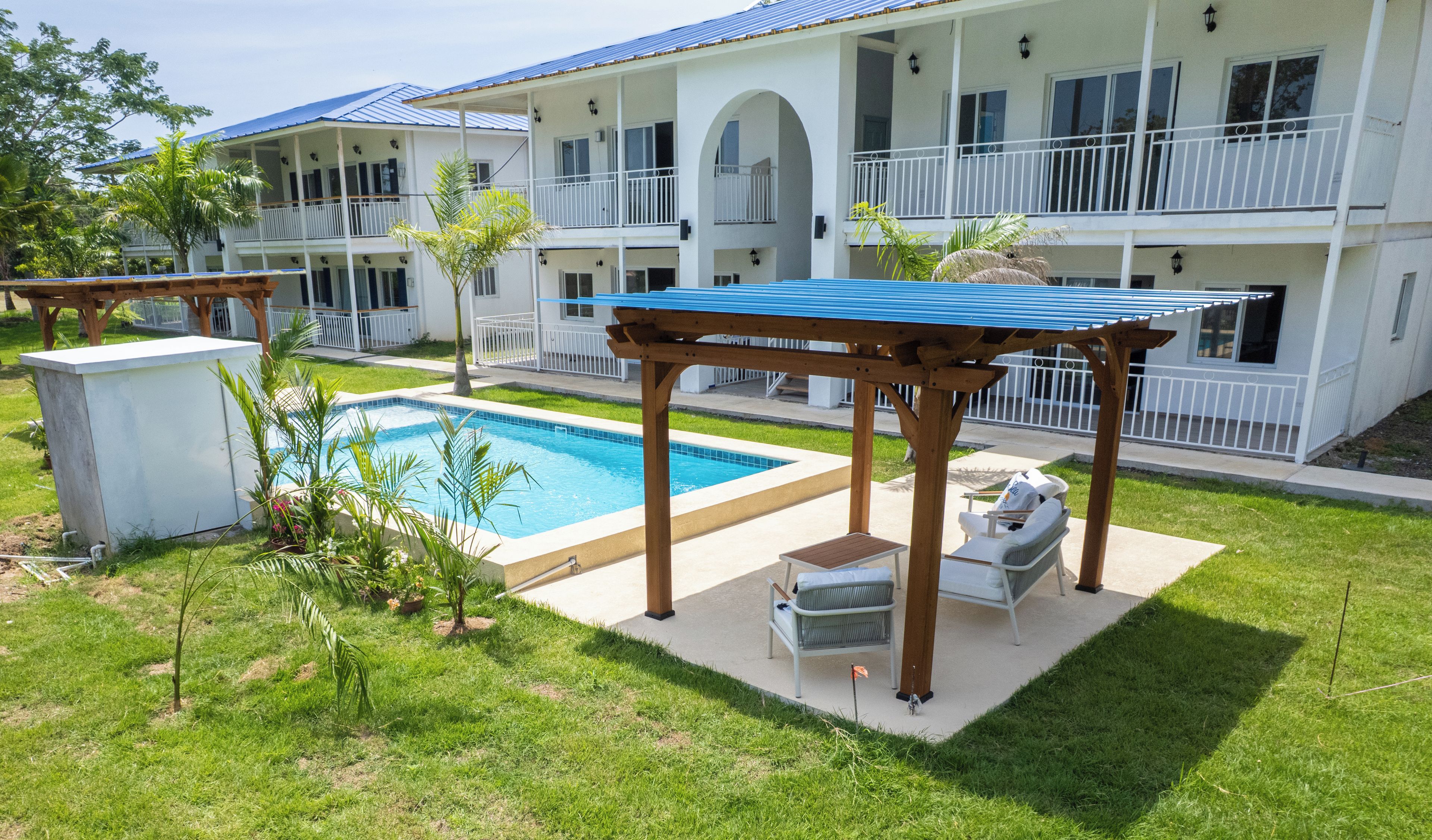 A pool area with a pergola, lounge chairs, and a building with balconies.