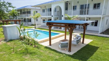 A pool area with a pergola, lounge chairs, and a building with balconies.