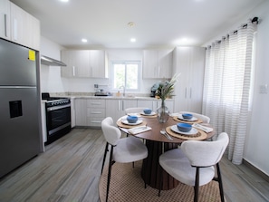 Una cocina moderna con comedor, electrodomésticos de acero inoxidable y una ventana con cortinas.