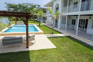 Un área de piscina con una pérgola, sillas de descanso y un edificio con balcones.