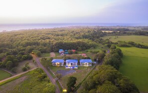 Un edificio grande con varias estructuras de techo azul, rodeado de exuberante vegetación y vistas al mar.