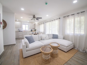 Una sala moderna con un sofá modular, dos mesas auxiliares tejidas y un ventilador de techo.