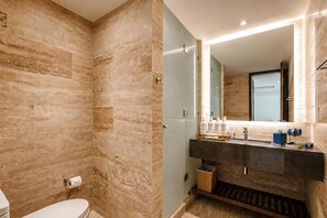 A modern bathroom with a marble wall, a glass shower enclosure, a vanity with a dark countertop, and a large mirror. - Tivoli Mérida Residences (Mérida)