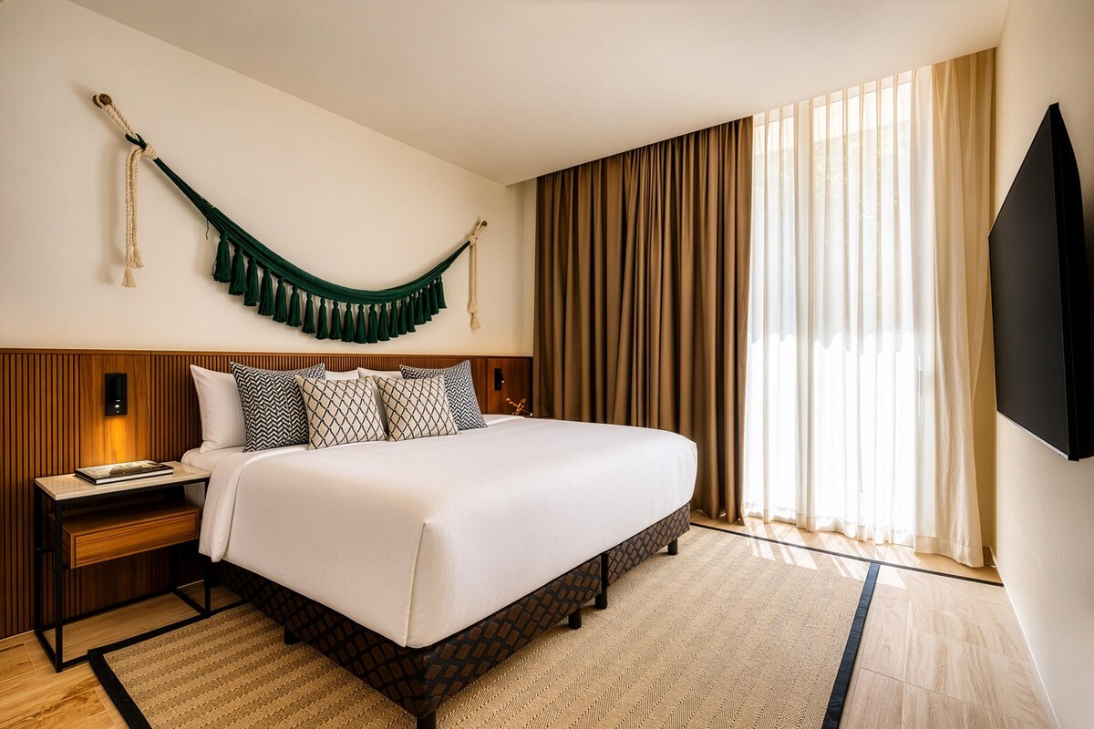 A hotel room with a bed, nightstand, TV, and a large window with curtains.