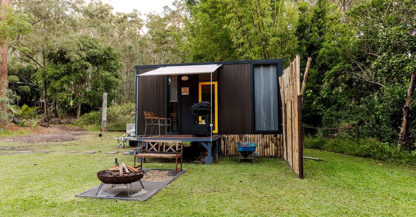 Uma cabana pequena com varanda, um local para fogueira e um carrinho de mão.