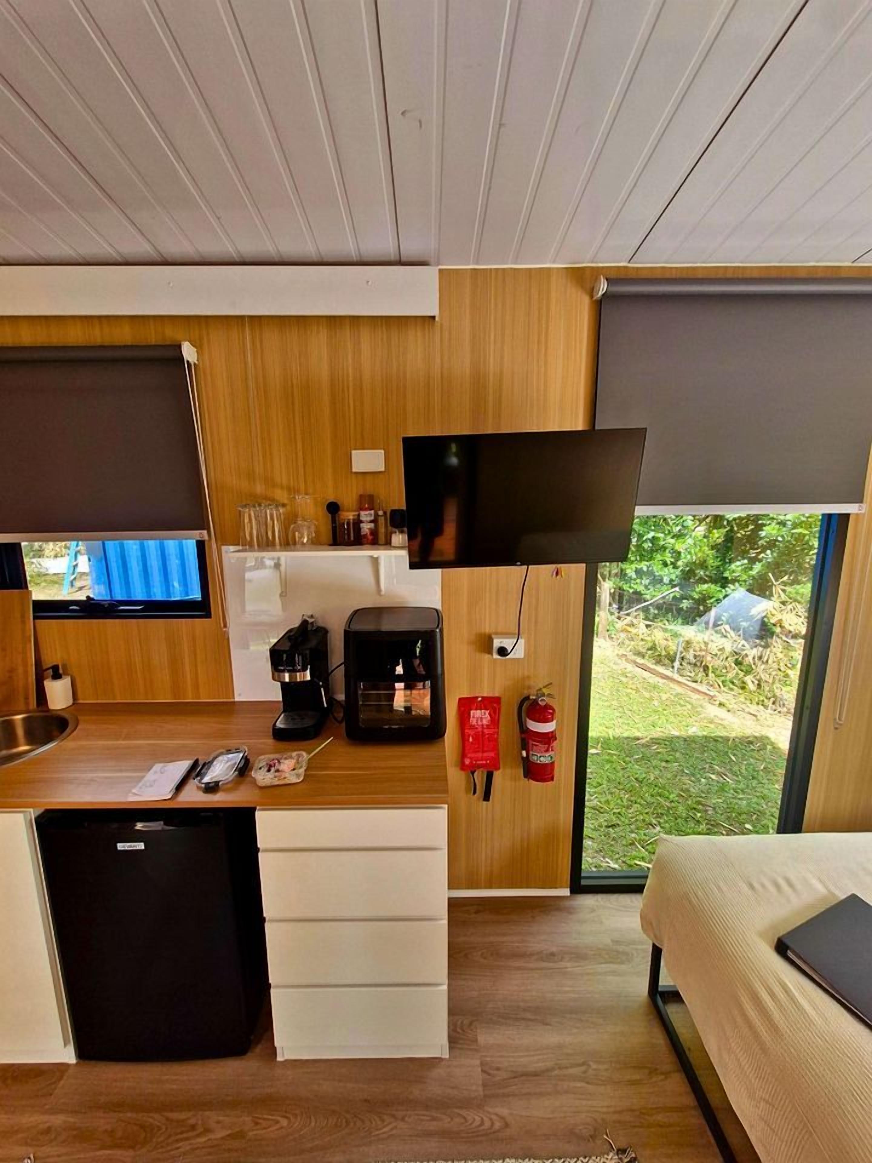 Quarto compacto com cozinha compacta, cama e janela com vista para o verde.