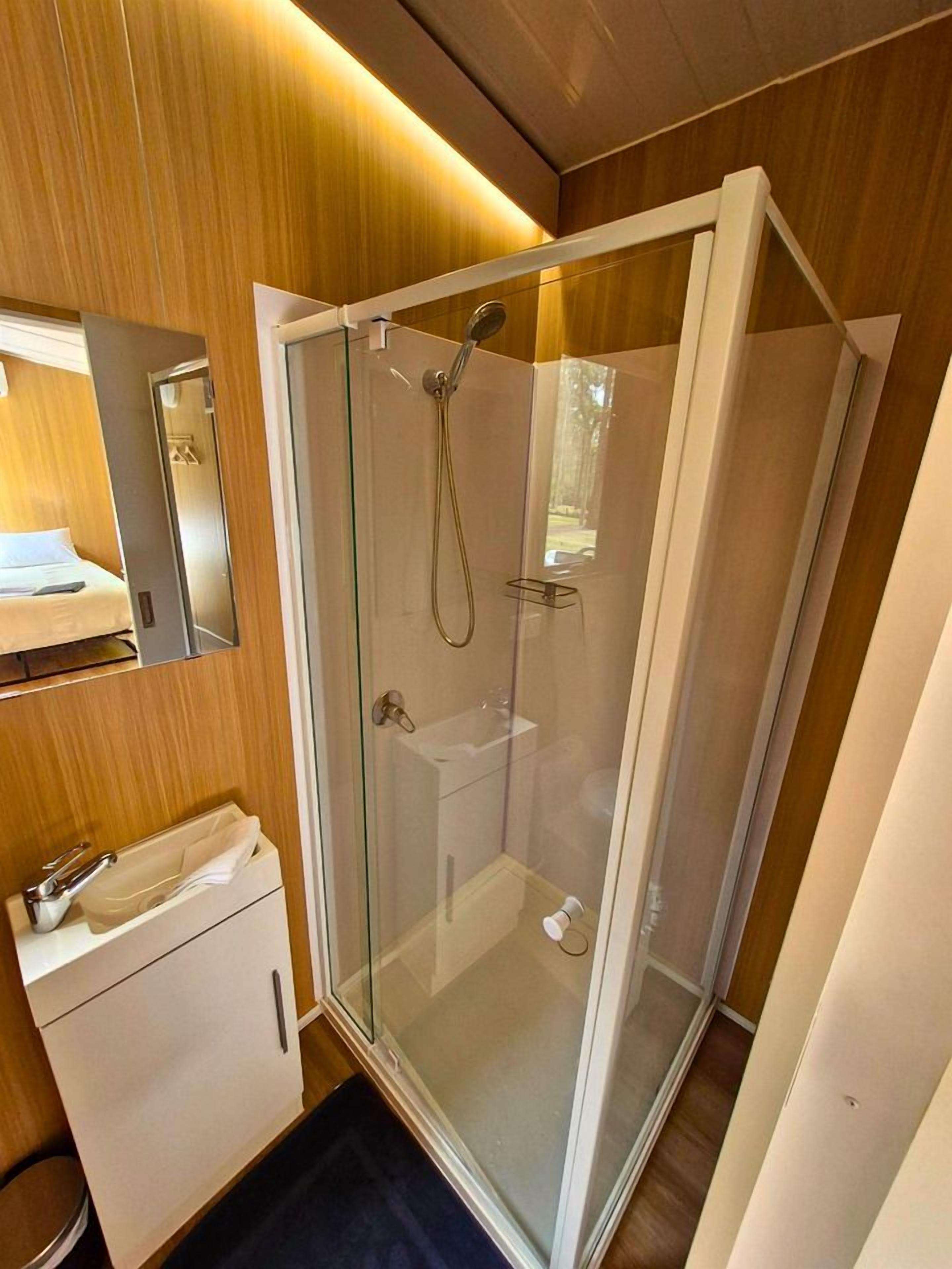 Une cabine de douche fermée par des parois en verre, dotée d’un pommeau de douche à main et d’un robinet fixé au mur.